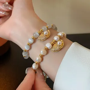 Close-up detailed view of cat's eye stone and pearl bracelets with gold seashell charms
