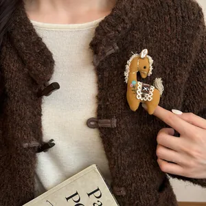 Vista dettagliata di una spilla pony in tessuto fatta a mano con ricamo su maglione marrone.