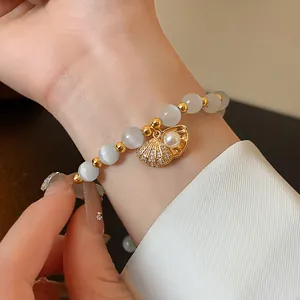 Close-up detail of a gold-plated cat's eye stone bracelet with a zircon shell charm and pearl