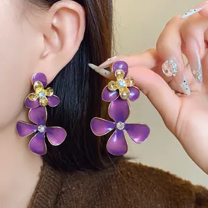 Close-up view of purple enamel flower drop earrings with rhinestones and gold finish