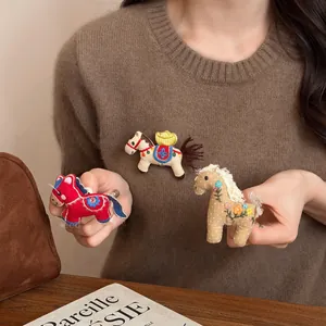 Dettaglio di tre spille fatte a mano in tessuto a forma di cavallino ricamato colorato.