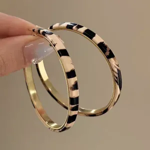 Chic leopard print leather hoop earrings with gold-toned metal and elegant silver needles.
