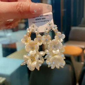 Close-up of elegant floral dangle earrings with zircon centers and white shell petals