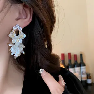 Detailed close-up of elegant shell flower drop earrings with zircon accents on model's ear.