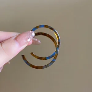 Detailed macro view of stylish tortoiseshell patterned hoop earrings held by a hand