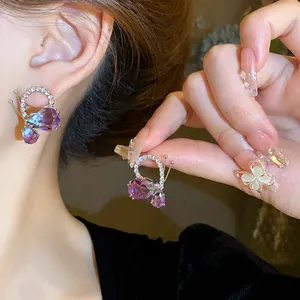 Close-up of elegant purple butterfly earrings with water drop crystals and shiny rhinestones.