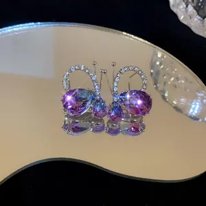Detailed close-up of butterfly waterdrop earrings with purple crystals on a mirror.