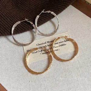 Eleganti orecchini a cerchio testurizzati oro e argento su uno sfondo di carta vintage