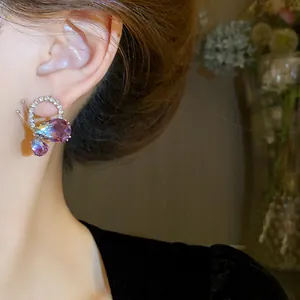 Close-up of elegant butterfly drop earrings with purple crystals on model's ear.
