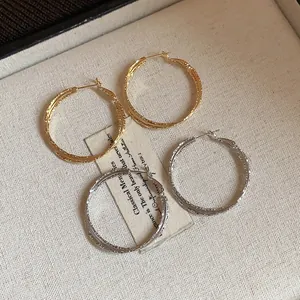 Dettaglio di orecchini a cerchio incrociati con perno in argento, oro e argento