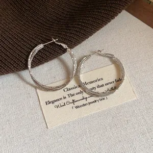 Dettaglio del design crossover testurizzato di orecchini a cerchio in argento su carta