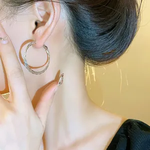 Primo piano di eleganti orecchini a cerchio in argento intrecciati indossati da una modella.