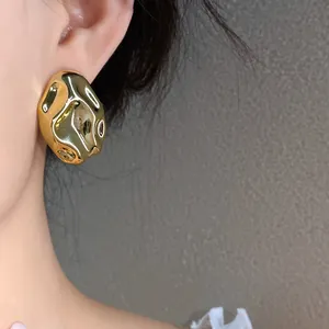 Primo piano di orecchini dorati a pieghe su una modella, design moderno a quadrato irregolare.