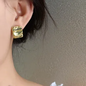 Primo piano di eleganti orecchini quadrati a pieghe color oro per un look moda femminile