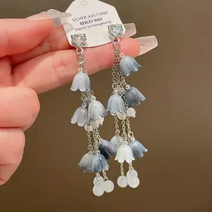 Gros plan de boucles d'oreilles à pompons avec fleurs bleues dégradées et cristaux brillants.