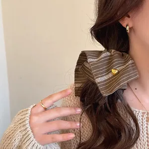 Detail view of a retro brown striped hair scrunchie featuring a gold heart-shaped charm