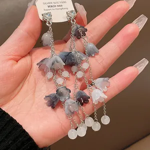 Détail rapproché d'élégantes boucles d'oreilles à pampilles fleuries bleues et argent.