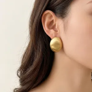 Orecchini a perno ovali in metallo dorato spazzolato minimalisti su modella donna