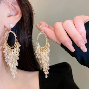 Close-up of elegant gold oval earrings with sparkling crystal tassels on model.
