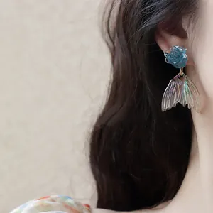 Close-up view of elegant iridescent mermaid tail dangle earrings featuring a blue rose stud