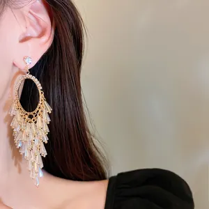 Close-up of elegant gold oval chandelier earrings with tiered crystal tassels on model.