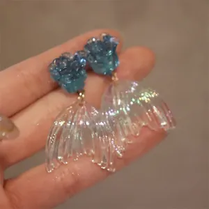 Detail shot showing the iridescent mermaid tail and blue rose studs of these elegant earrings