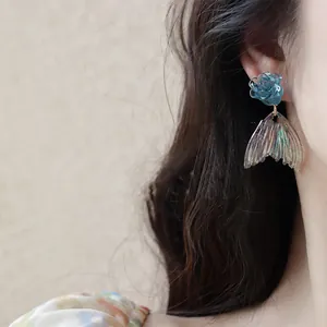 Detailed macro shot of blue rose and iridescent fish tail drop earrings worn on an ear