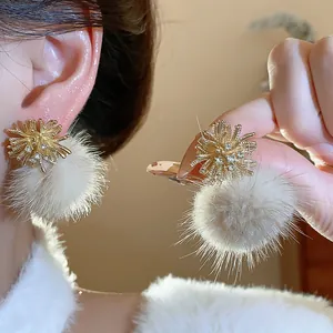 Close-up detail of elegant gold firework-shaped earrings with soft cream faux fur pom-poms