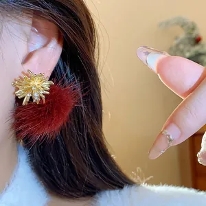 Detailed view of festive gold firework stud earrings featuring a plush deep red fur pom-pom.