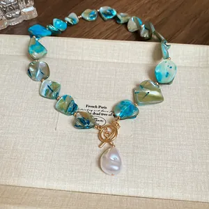 Detail of irregular iridescent glass beads and baroque pearl pendant on gold OT buckle necklace