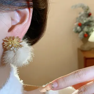 Close-up detail of a elegant gold firework earring with white fur ball worn on an ear.