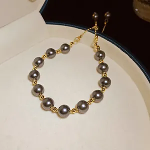 Dettaglio delle perle grigie e sfere dorate su un bracciale regolabile