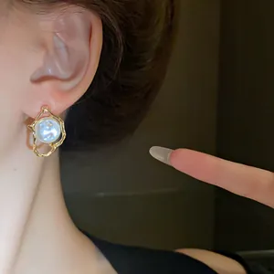 Macro view of an irregular gold-tone earring featuring a central white pearl inlay