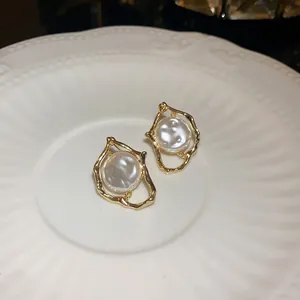 Detailed view of retro irregular gold earrings with center pearls on a white plate