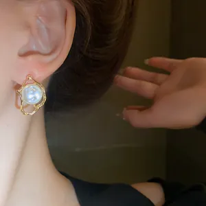 Detailed view of a vintage irregular golden frame pearl stud earring worn on a model's ear