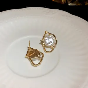 Close-up detail of irregular gold-framed pearl earrings showing front and back textures
