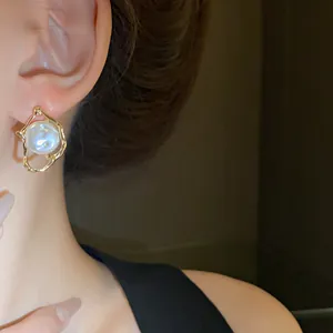 Detailed view of elegant irregular gold-framed pearl stud earrings worn on a model ear lobe.