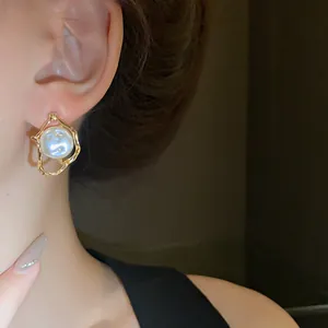 Close-up of vintage irregular gold earrings with pearl inlay worn by a female model