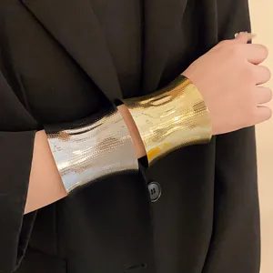 Macro view of textured gold and silver metal wide cuff bracelets worn with black blazer