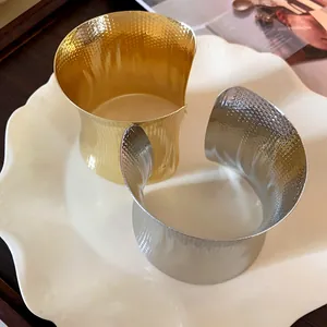Macro view of wide hammered gold and silver open cuff bracelets on a cream plate