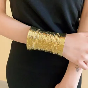 Detailed view of a wide gold cuff bracelet with intricate floral embossing on model's wrist