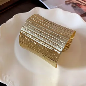 Close-up of wide gold open cuff bracelet with horizontal ribbed texture on white plate.
