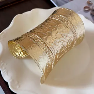 Detailed view of wide gold cuff bracelet with intricate embossed floral patterns