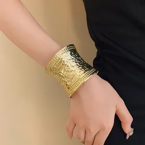 Macro view of wide gold open cuff bracelet featuring intricate embossed floral textures