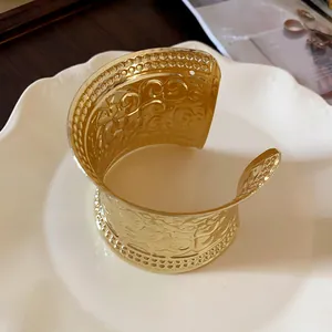 Close-up of wide gold cuff bracelet with intricate vintage floral embossing on a plate.