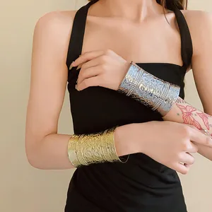 Detail view of gold and silver engraved metal cuff bracelets on a model wearing black.