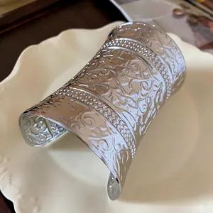 Detail of a wide silver-tone cuff bracelet with intricate floral engravings on a plate.