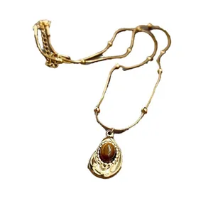 Elegant gold necklace featuring an oval faux tiger-eye stone in a teardrop pendant.