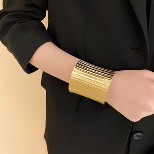 Close-up of a wide gold ribbed cuff bracelet worn with a professional black blazer