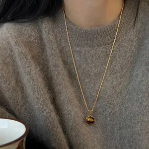 Detailed view of a Maillard style tiger eye stone pendant necklace on a cozy brown sweater